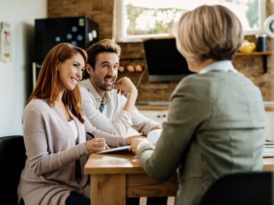 Young happy couple signing lease agreement on a meeting with real estate agent. Happy woman signing a document while being with her husband on a meeting with insurance agent.